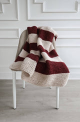 Cream and dark red knit blanket on a dining chair, in front of a white wall with trim details.  thumbnail