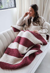 Woman lounging on a cream couch with a garter stitch striped blanket on her lap.  thumbnail