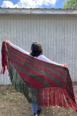 Woman holds shawl extended behind her, with arms outstretched. The shawl is longer than her wingspan along the top and has long fringe on the lower edge. It is striped in wine red and pine green.  thumbnail
