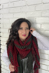 Woman leans against white painted brick wall with large knit shawl wrapped bandana style.  thumbnail
