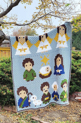Crochet C2C afghan draped over tree branch in a backyard. The afghan has a pale blue background with cartoon-style figures.  thumbnail