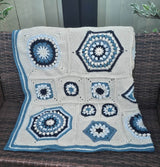 Crochet afghan laid over wicker outdoor couch, showing varied block sizes and striped border.  thumbnail