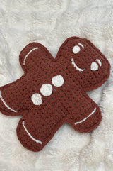 Close up of pillow laid on cream background, showing white embellishments for face, buttons, and lines as wrists and feet of gingerbread person.  thumbnail