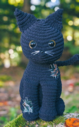 Crochet black cat, sitting upright with pointed ears and a skinny tail. It has shiny plastic eyes and nose, and embroidered whiskers.  thumbnail