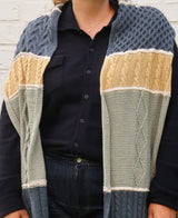 Cropped front view of knit scarf worn draped over shoulders. Each color black section has a different cable motif.  thumbnail