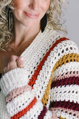 Close up of left shoulder and cuff, with model's arm raised, showing texture in crochet body and ribbed front band and sleeve hem.  thumbnail