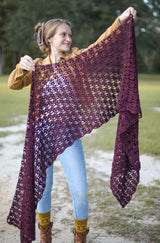 Woman holds lacy crochet wrap toward camera, showing open texture.  thumbnail