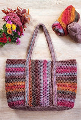 Crochet tote bag laid on pale wooden surface, with two balls of yarn in the upper right corner and a bouquet of fall flowers in the upper left corner.  thumbnail