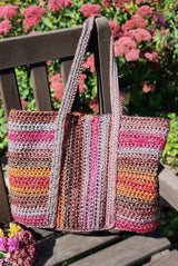 Tote bag sits on wooden chair in backyard, with dark mauve flowers in the background. The bag has shoulder length handles.  thumbnail