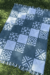 Top down view of crochet blanket laid flat on grass. The blanket has solid squares and patterned squares in 4 motifs.  thumbnail