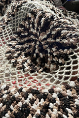 Crochet blanket draped over legs, showing open textures of mesh section in worsted weight yarn.  thumbnail