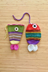 Two crocheted pouches in the shape of fish lay on a pale bamboo background. The fish pouches have a drawstring top and two fins at the bottom.  thumbnail
