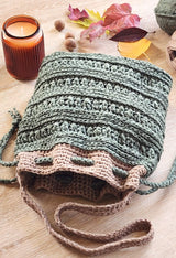 Front view of crochet bag, showing opening with drawstring. The bag is made in olive with a textured stitch, and has a top edge and shoulder strap in tan.  thumbnail