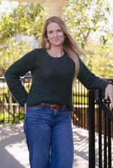 Woman in a long sleeve crochet sweater and jeans stands on a porch. The sweater is a dark green.  thumbnail