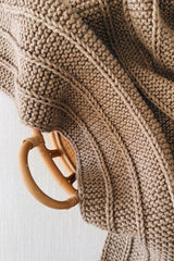Close up top down view of knit blanket with garter stitch and columns of a single stockinette stitch. The blanket is laid in a basket on a white background.  thumbnail