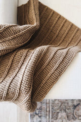 Top down view of knit throw draped over arm of white couch. The blanket is made in a warm brown.  thumbnail