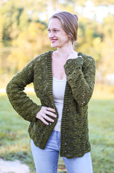 Woman in a green crochet cardigan woen over cream tank top and jeans, standing in a grassy yard.  thumbnail