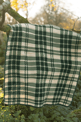 Crochet plaid blanket draped over tree limb. The blanket is made in beige, pale green, and darker green.  thumbnail