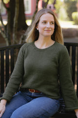 Woman in an olive green sweater and jeans sits on a a park bench.  thumbnail