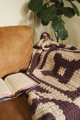 Crochet lapghan laid over arm of couch. The afghan is made in tan and dark plum, with a geometric design. thumbnail