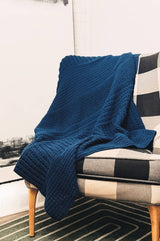 Crochet afghan in a rich blue draped over a black & white gingham chair, in a living room corner.  thumbnail