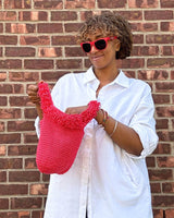 Woman in sunglasses holding open crochet bag in front of a brick wall.  thumbnail