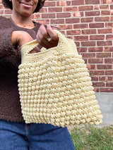Woman holding butter yellow crochet bag with bobble stitches  in front of brick wall thumbnail