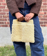 Woman holding butter yellow crochet bag with bobble stitches  in front of brick wall thumbnail