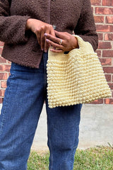 Woman holding butter yellow crochet bag with bobble stitches  in front of brick wall thumbnail