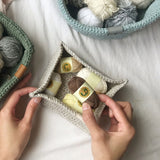 Hand holding a mini skein of yarn above a tray with other mini skeins thumbnail