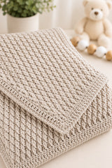 Neutral baby blanket folded on white flat surface with toys in the background thumbnail
