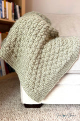 olive green knitted seersucker throw blanket draped over the arm of a beige armchair thumbnail