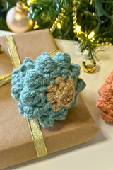 handmade teal bobble stitch Christmas tree ornament resting on a wrapped gift thumbnail