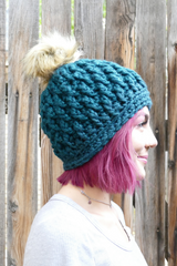 person wearing a teal alpine stitch crochet beanie with a faux fur pom pom outdoors thumbnail