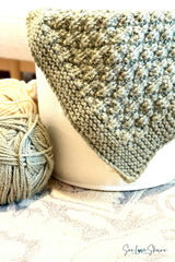 close-up of sage green knitted seersucker blanket folded over a white bucket next to a skein of yarn thumbnail