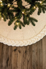 cream knitted Christmas tree skirt with a braided cable border flat laid on dark wood thumbnail