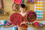 young boy holding up jumbo lollipop crafts surrounded by candy themed decorations thumbnail