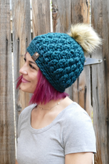 person wearing a teal alpine stitch crochet beanie with a faux fur pom pom outdoors thumbnail