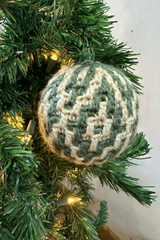 handmade argyle mosaic crochet Christmas ornament hanging on a pine tree with fairy lights thumbnail