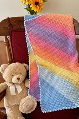 handmade pastel C2C Suzette stitch baby blanket draped over a red chair next to a teddy bear and flowers thumbnail