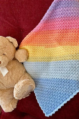 close-up of handmade pastel C2C Suzette stitch baby blanket draped over a red chair next to a teddy bear thumbnail