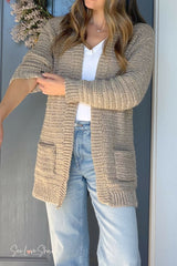 person wearing a beige crochet cardigan jeans and white shirt standing near a blue door thumbnail