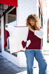 Woman wearing sweater with heart pocket holding up a second sweater in alternate colors thumbnail