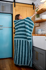 Girl wrapped in striped blanket reaching for something on a shelf thumbnail
