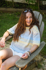 Model sitting in chair wearing a multicolor striped tee with mid length sleeves thumbnail