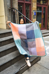 Woman on city steps holding a color blocked crochet blanket up thumbnail