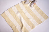 baby on knit yellow and cream striped blanket in front of a white background thumbnail