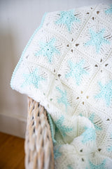 Close up of white granny square blanket with blue glow in the dark stars and border on a chair thumbnail