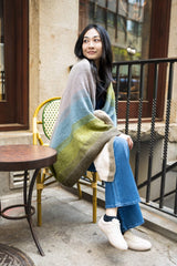 woman wrapped in colorful knit blanket sitting at a table thumbnail