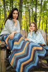 Two women in the woods with a multicolor crochet blanket on their laps.  thumbnail